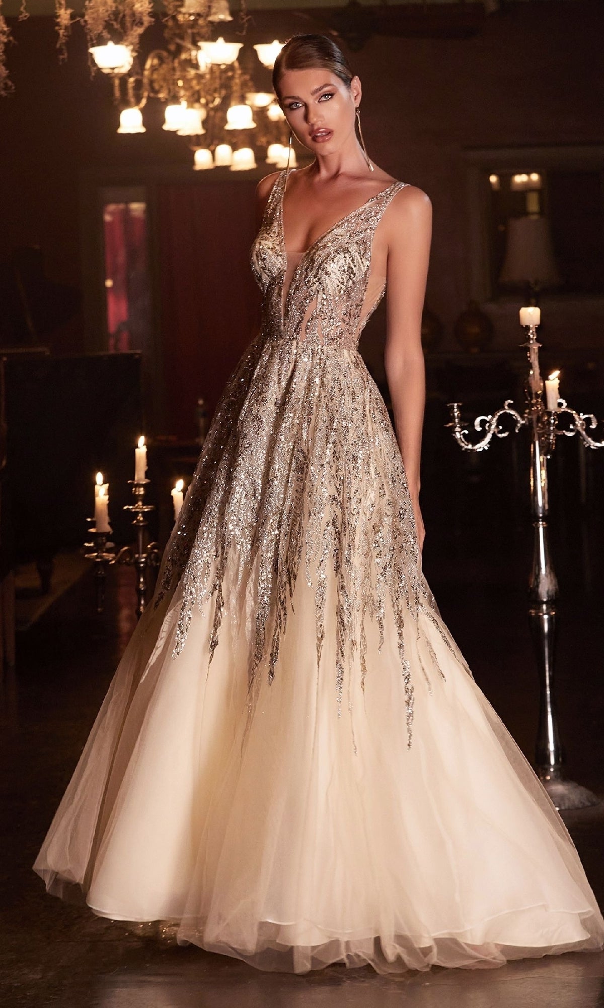 A woman stands indoors, illuminated by candlelight, wearing the Ladivine C135 Sheer-Sides Long Glitter Prom Dress with a fitted deep V-neck bodice, silver sequins, and a full tulle skirt.